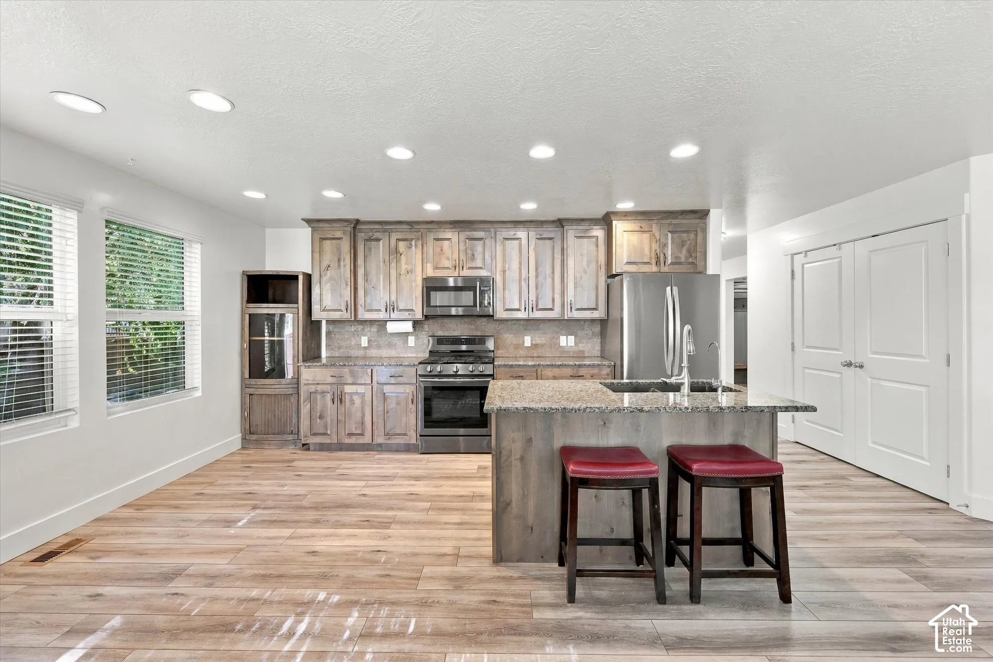 Kitchen featuring wood-finish cabinetry, stone-surface countertops, stainless steel appliances, wood-finish flooring, and recessed lighting