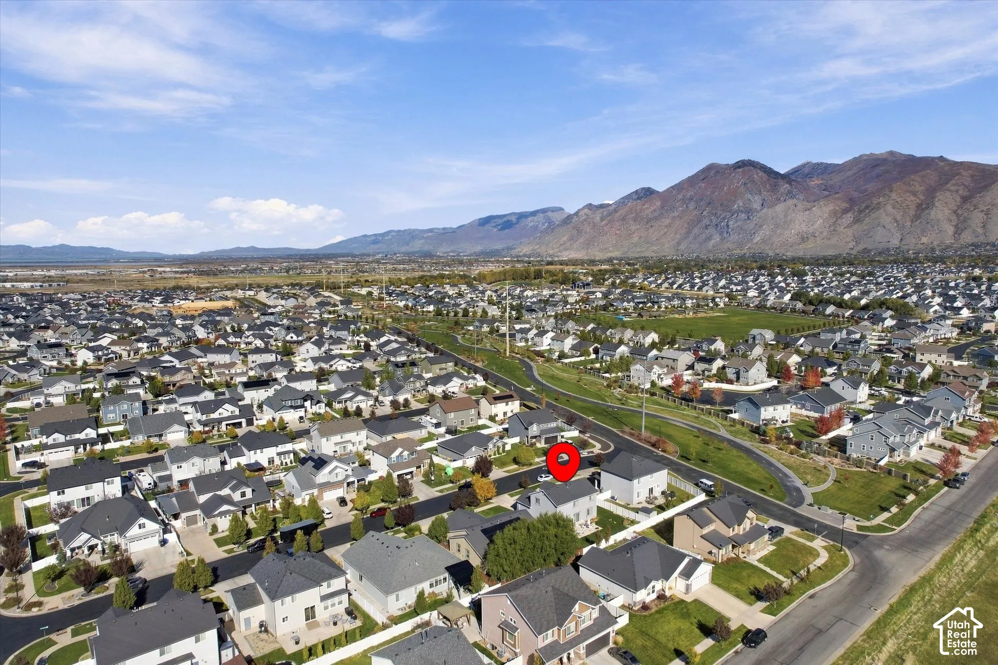 Aerial perspective of a multi-story residential property featuring a neutral exterior, multi-pitched roofline, and proximity to expansive mountain backdrops