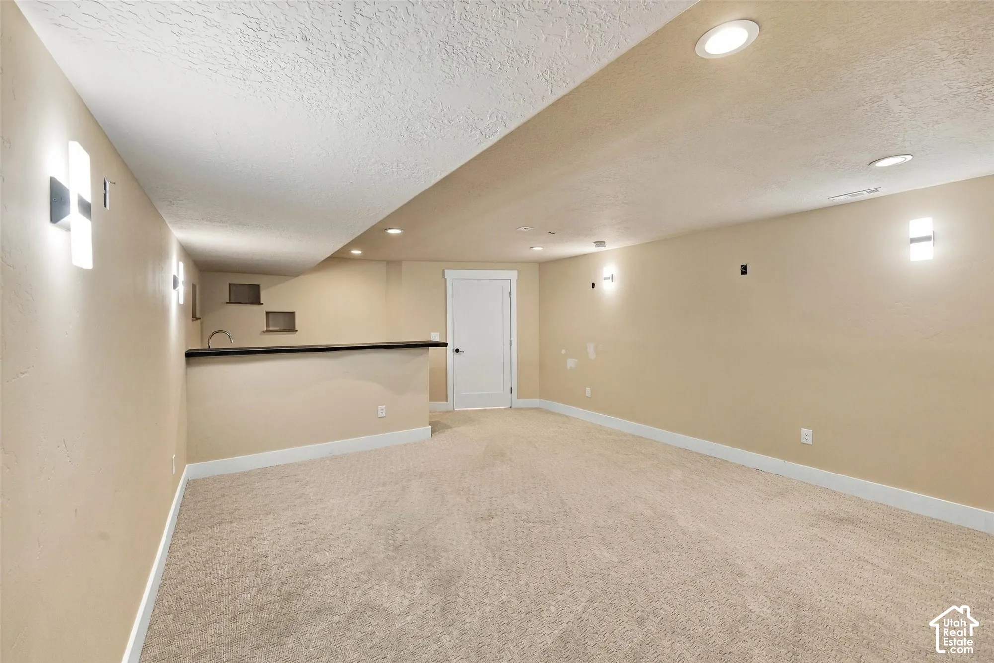Neutral-toned room featuring recessed lighting, wall-mounted light fixtures, wall-to-wall carpeting, and a built-in wet bar with a countertop