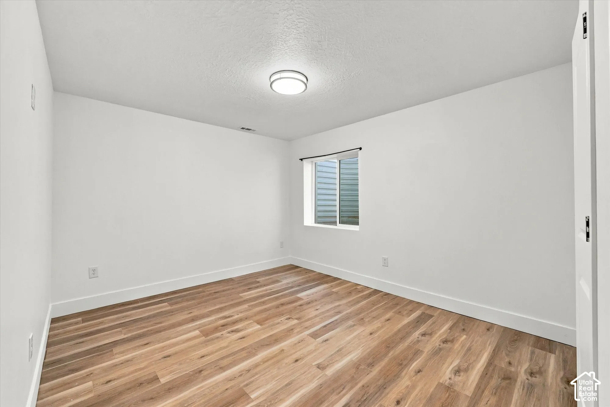 Neutral room featuring wood-finish flooring, white walls, and a ceiling-mounted flush light fixture