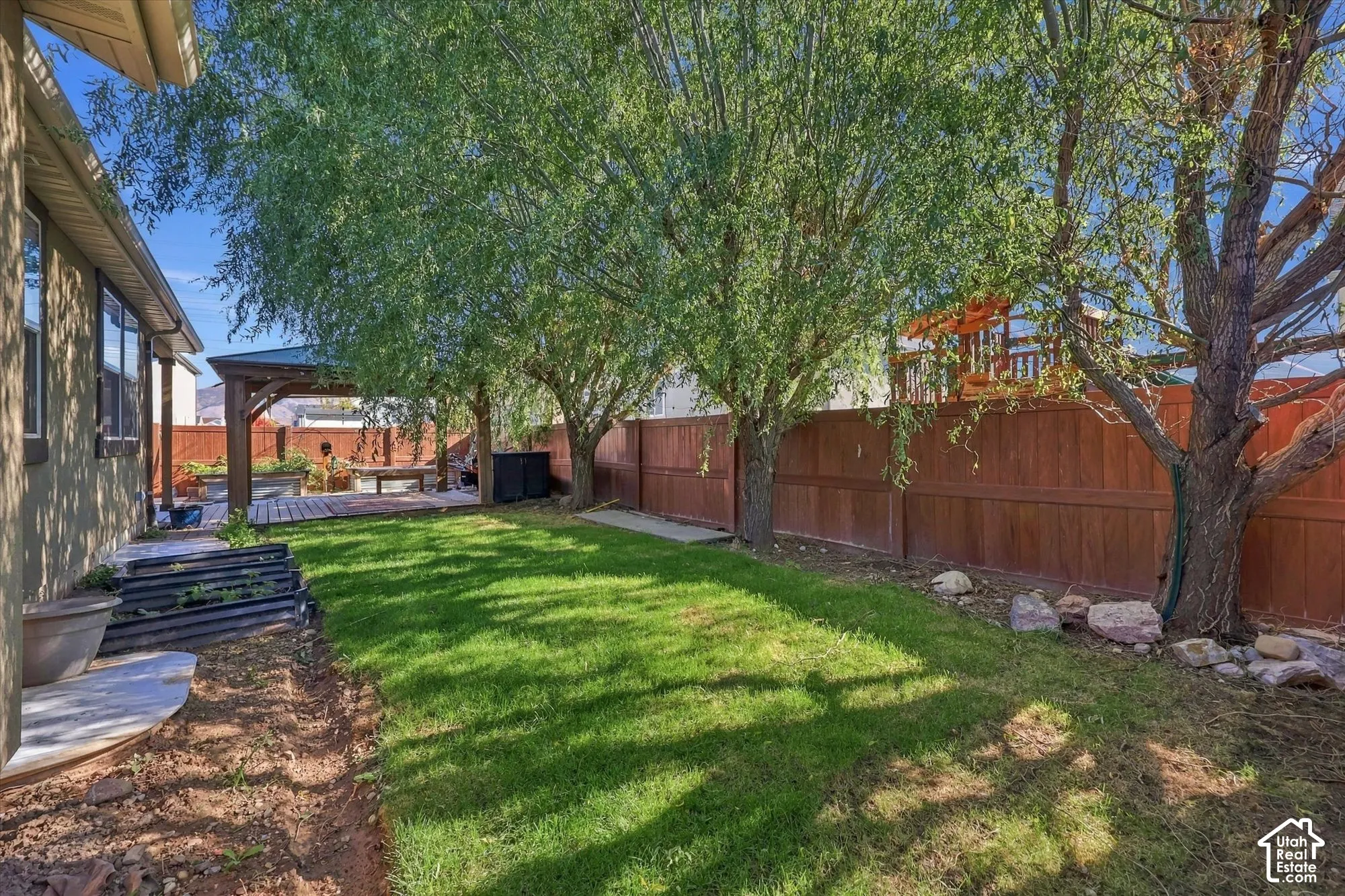 Rear yard featuring a manicured lawn, wood-privacy fencing, mature shade trees, and a covered timber-framed patio structure