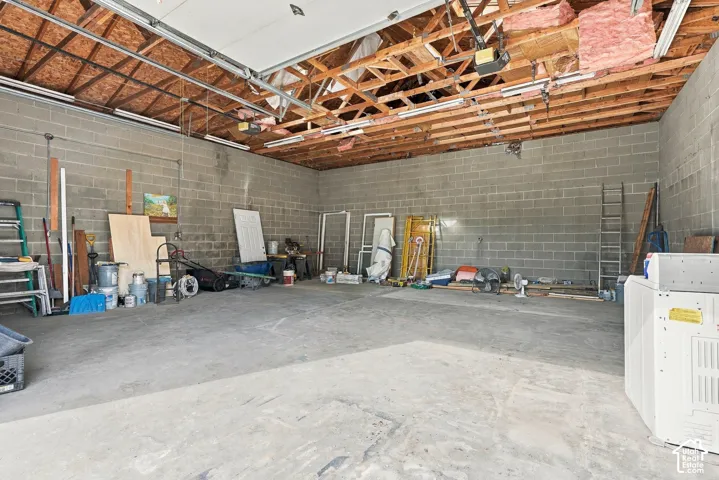 Spacious multi-car garage featuring exposed wood truss ceiling, concrete block walls, and concrete flooring