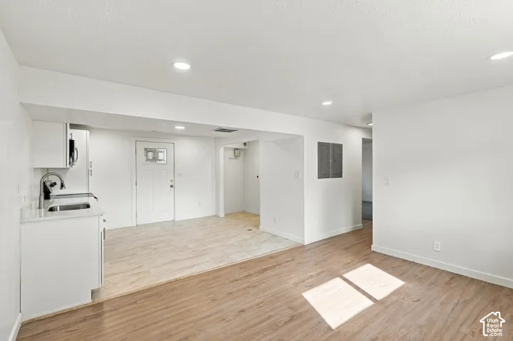 Kitchenette area featuring white cabinetry, solid-surface countertops, an undermount sink with a gooseneck faucet, recessed lighting, and wood-finish flooring