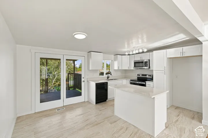 Kitchen featuring white cabinetry, stone-finish countertops, stainless steel appliances, a central island, and double glass doors