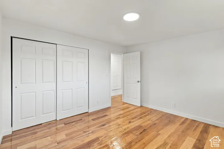 Room featuring wood-finish flooring, white walls, flush-mount ceiling lighting, six-panel closet doors, and a six-panel door