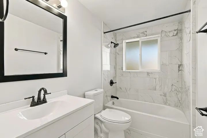 Bathroom featuring a vanity with a white countertop and oval sink, wall-mounted matte black faucet, framed mirror, and a tub-shower combination with floor-to-ceiling stone-look tile surround and matte black fixtures