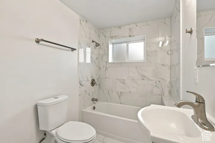 Bathroom featuring large-format tile shower surround with stone-pattern finish, soaking tub, pedestal sink with brushed-nickel faucet, and a wall-mounted towel bar