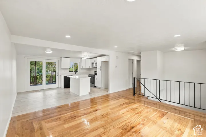 Open-concept kitchen and living area featuring wood-finish flooring, a central island, recessed lighting, and white cabinetry