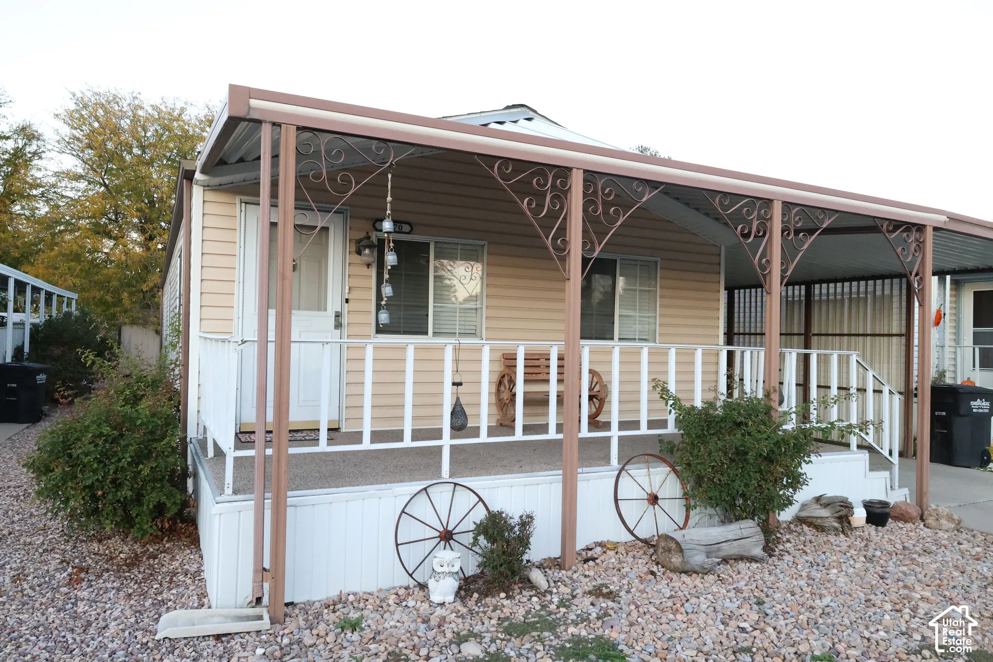 Exterior featuring light-colored horizontal siding, a covered front porch with ornate metal supports, a white railing, and a side carport