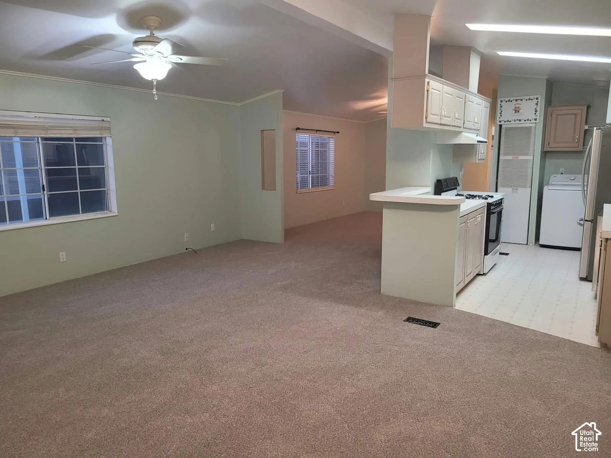 Open concept interior featuring wall-to-wall carpeting, a ceiling fan with integrated lighting, a peninsula counter with cabinetry, and multi-pane windows