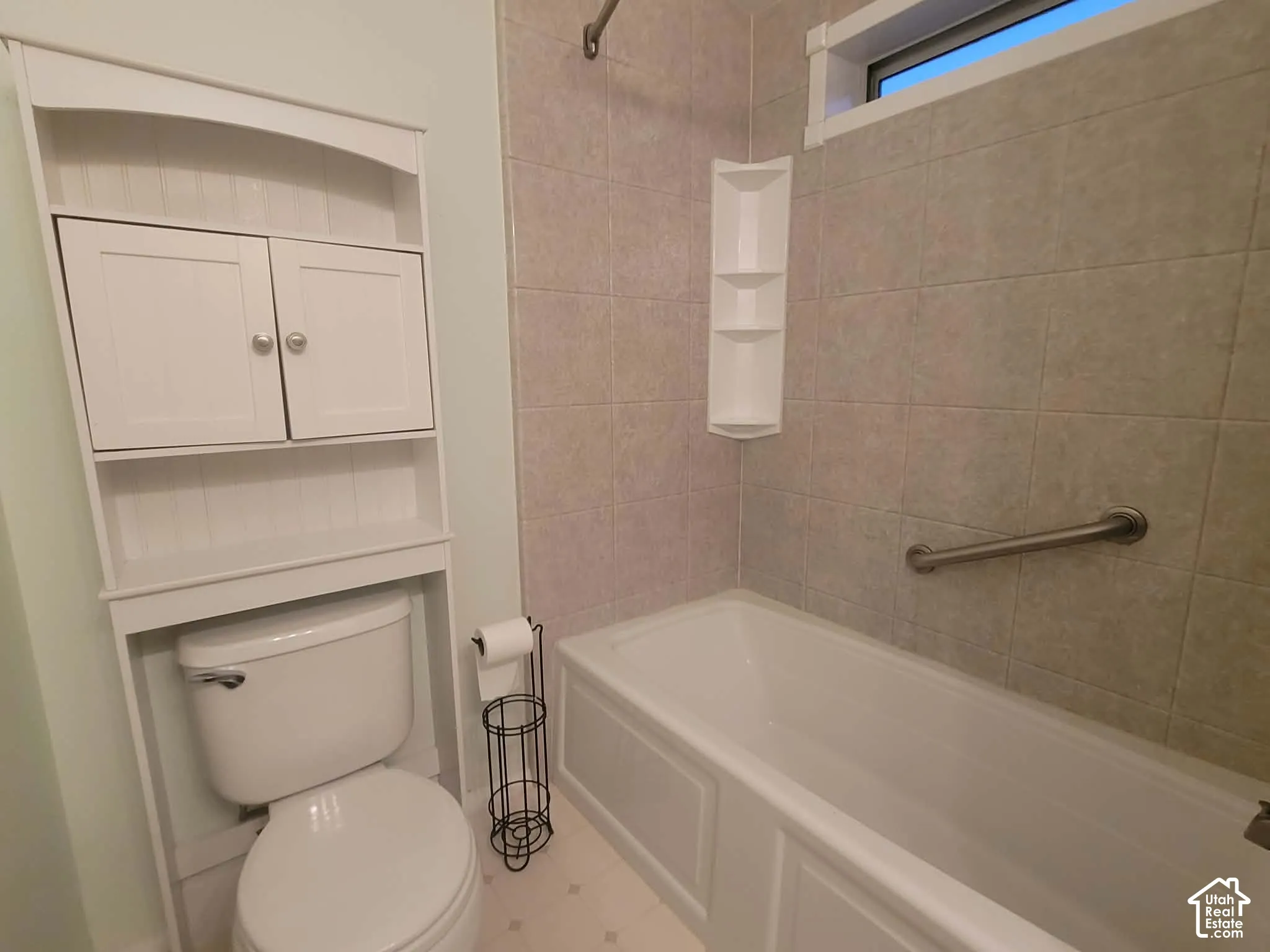 Full bathroom (in Hall) featuring a white bathtub with tile surround, built-in shelving, a stainless steel grab bar, and white over-the-toilet storage cabinetry