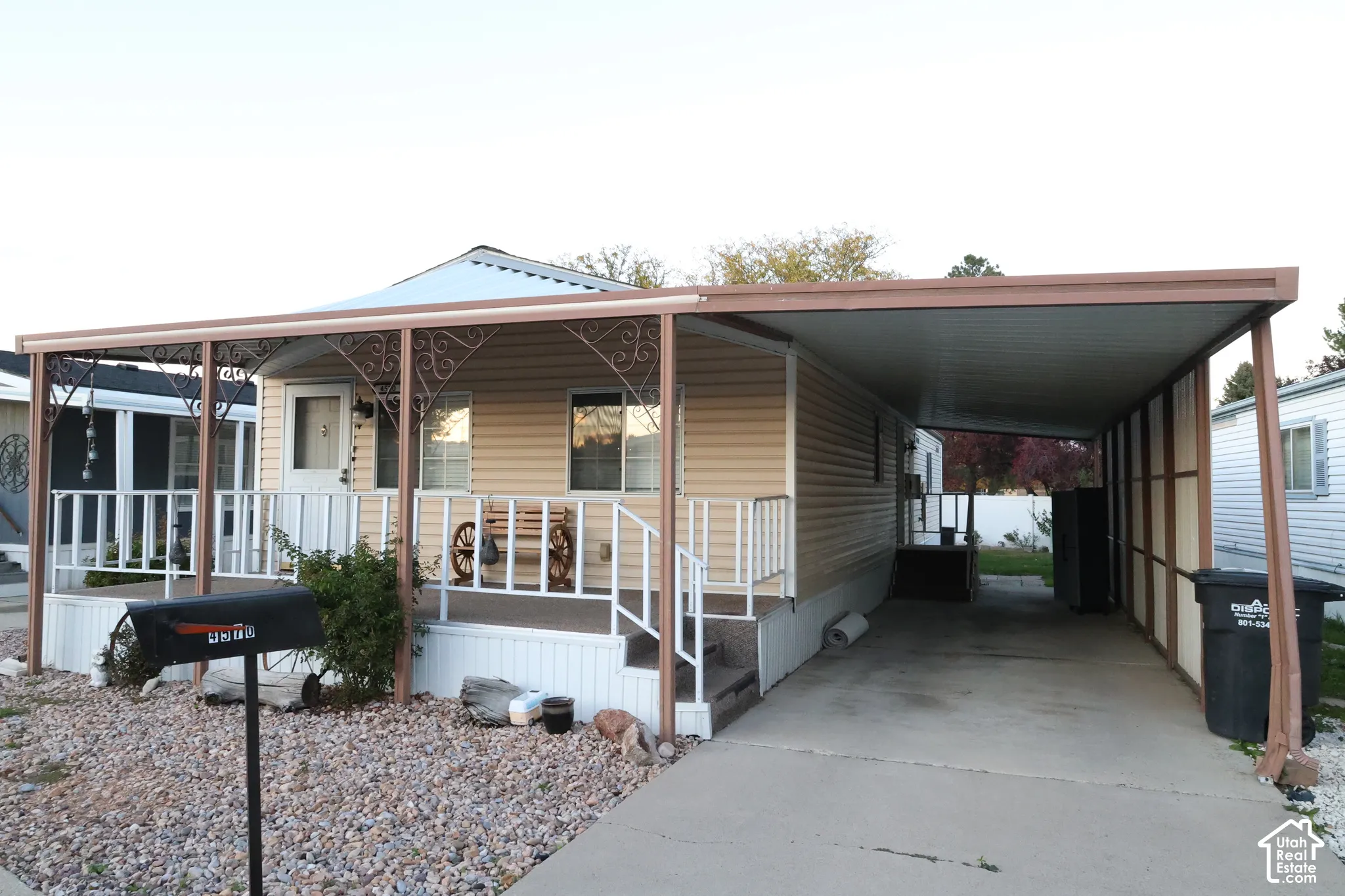 Exterior featuring light-colored horizontal siding, a covered front porch with decorative wrought iron accents, white railings, and an attached metal-roofed carport