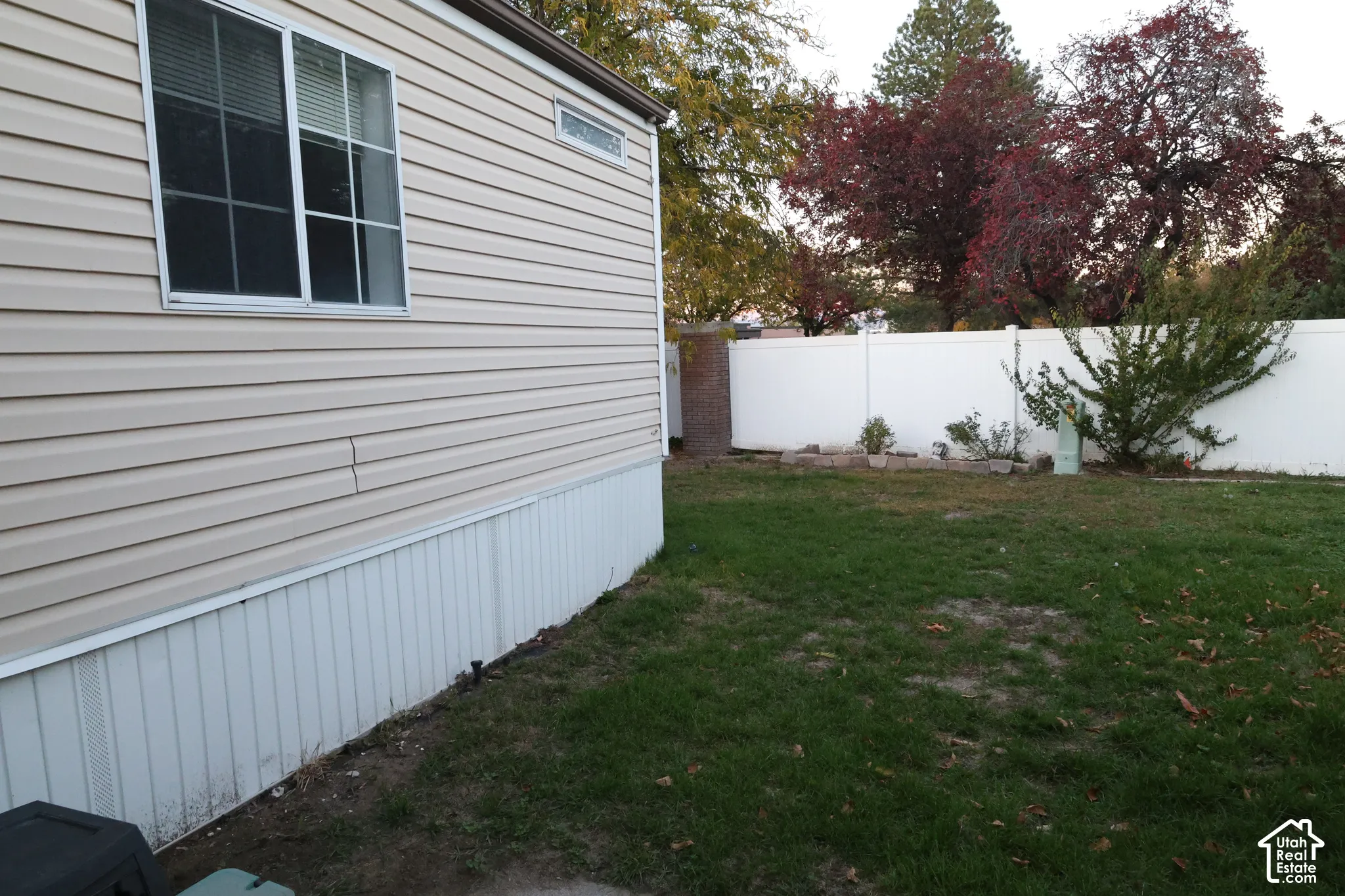 Exterior side profile featuring light-toned horizontal siding, a white vinyl privacy fence, and a grass-covered backyard