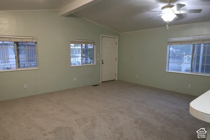 Vaulted ceilings, carpeted flooring, multiple windows with grid detailing, and a central ceiling fan with integrated light fixture