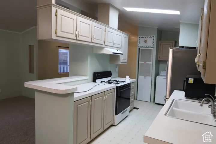 Kitchen featuring a peninsula counter, upper and lower shaker-style cabinetry, a dual-basin sink, and a built-in range hood
