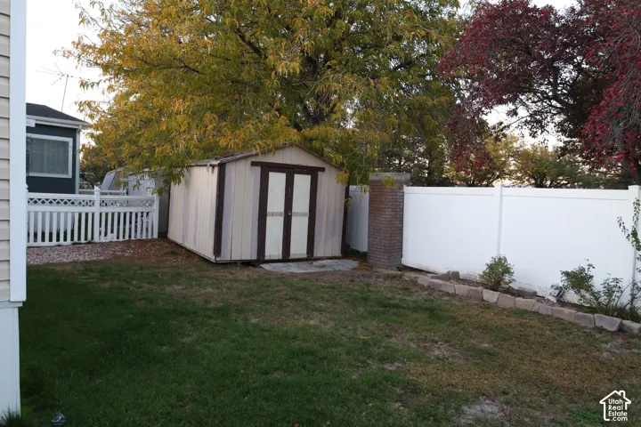 Backyard featuring a white vinyl privacy fence, storage shed, brick pillar, and stone garden edging