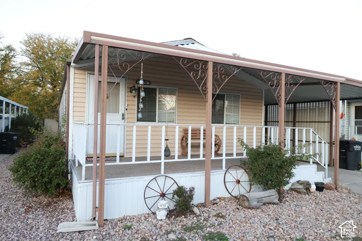 Exterior featuring light-colored horizontal siding, a covered front porch with ornate metal supports, a white railing, and a side carport