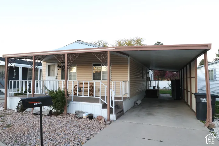 Exterior featuring light-colored horizontal siding, a covered front porch with decorative wrought iron accents, white railings, and an attached metal-roofed carport