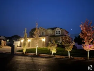 Two-story residence featuring a multi-gabled roofline, lap siding, concrete driveway, and a front lawn with mature deciduous trees
