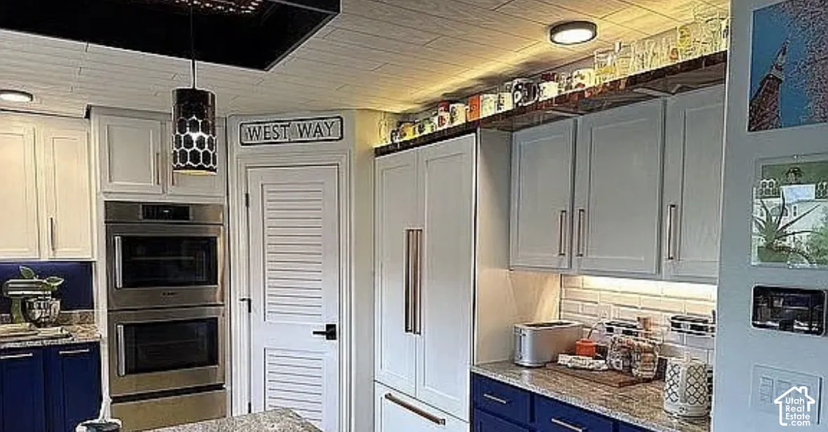 Kitchen featuring shaker-style cabinetry in navy and white, stone countertops, stainless steel double wall ovens, white subway tile backsplash, and paneled refrigerator front