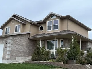 Two-story residence featuring a tan stucco and brick facade, a covered front porch with white railing, and decorative arched and circular window detailing