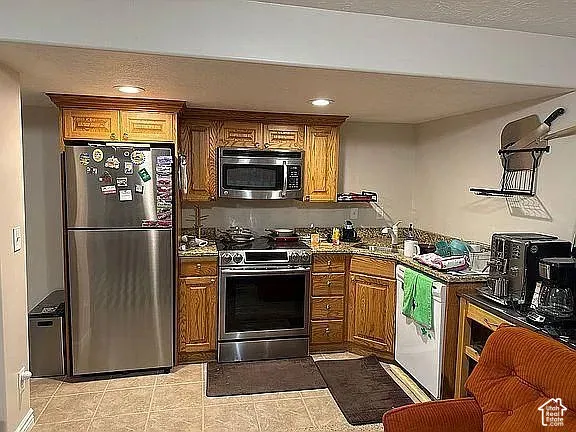 Kitchen featuring stained wood cabinetry, stone countertops, stainless steel refrigerator, built-in microwave, and range