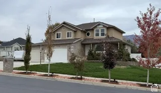 Two-story residence featuring a dual-tone exterior of stone veneer and stucco, a multi-car garage, and a manicured front lawn
