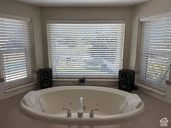 Oval soaking tub featuring integrated hydrotherapy jets, dual contoured headrests, and a center-mounted faucet set, recessed into a spacious deck with triple-window bay configuration and adjustable horizontal blinds