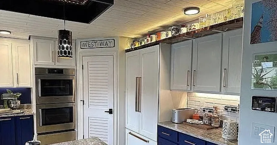 Kitchen featuring shaker-style cabinetry in navy and white, stone countertops, stainless steel double wall ovens, white subway tile backsplash, and paneled refrigerator front