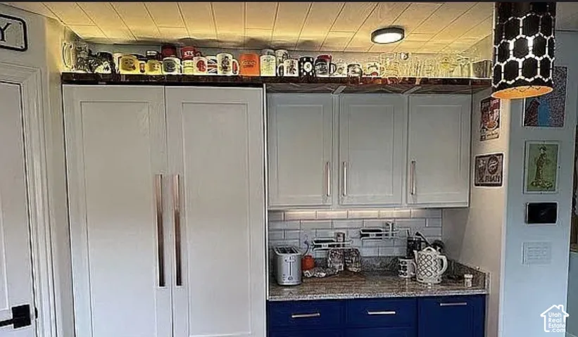 Kitchen area featuring floor-to-ceiling cabinetry, white subway tile backsplash, stone-finish countertops, contrasting base cabinets, and paneled refrigerator housing