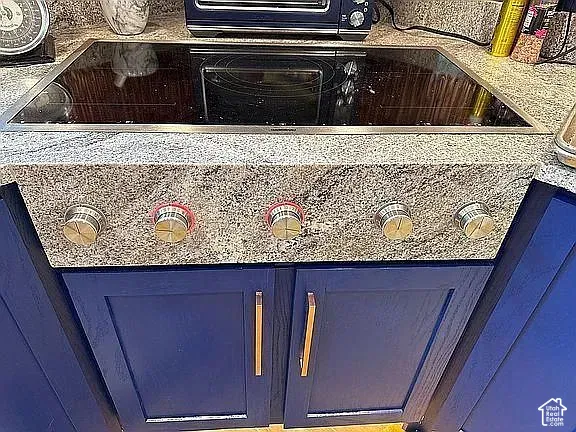 Electric glass cooktop inset into a natural stone countertop with blue shaker-style cabinetry and metallic hardware