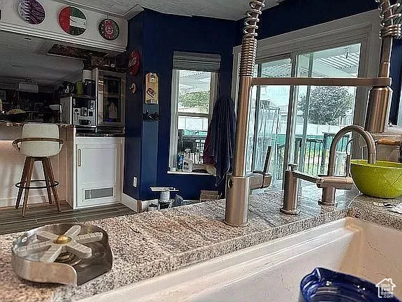 Kitchen area featuring a large apron-front sink, industrial-style high-arc faucet, integrated glass rinser, and stone countertop