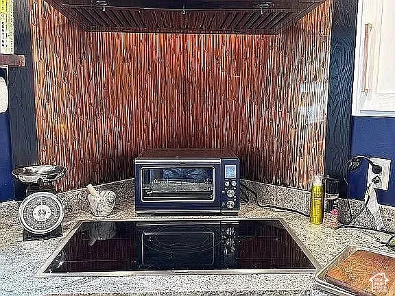 Textured copper-finish backsplash featuring a built-in dark metal range hood, smooth-surface electric cooktop, and stone-finish countertop