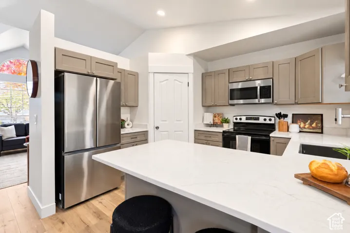 Kitchen featuring a central island with a solid surface countertop, wood-finish flooring, shaker-style cabinetry, stainless steel appliances, and vaulted ceilings