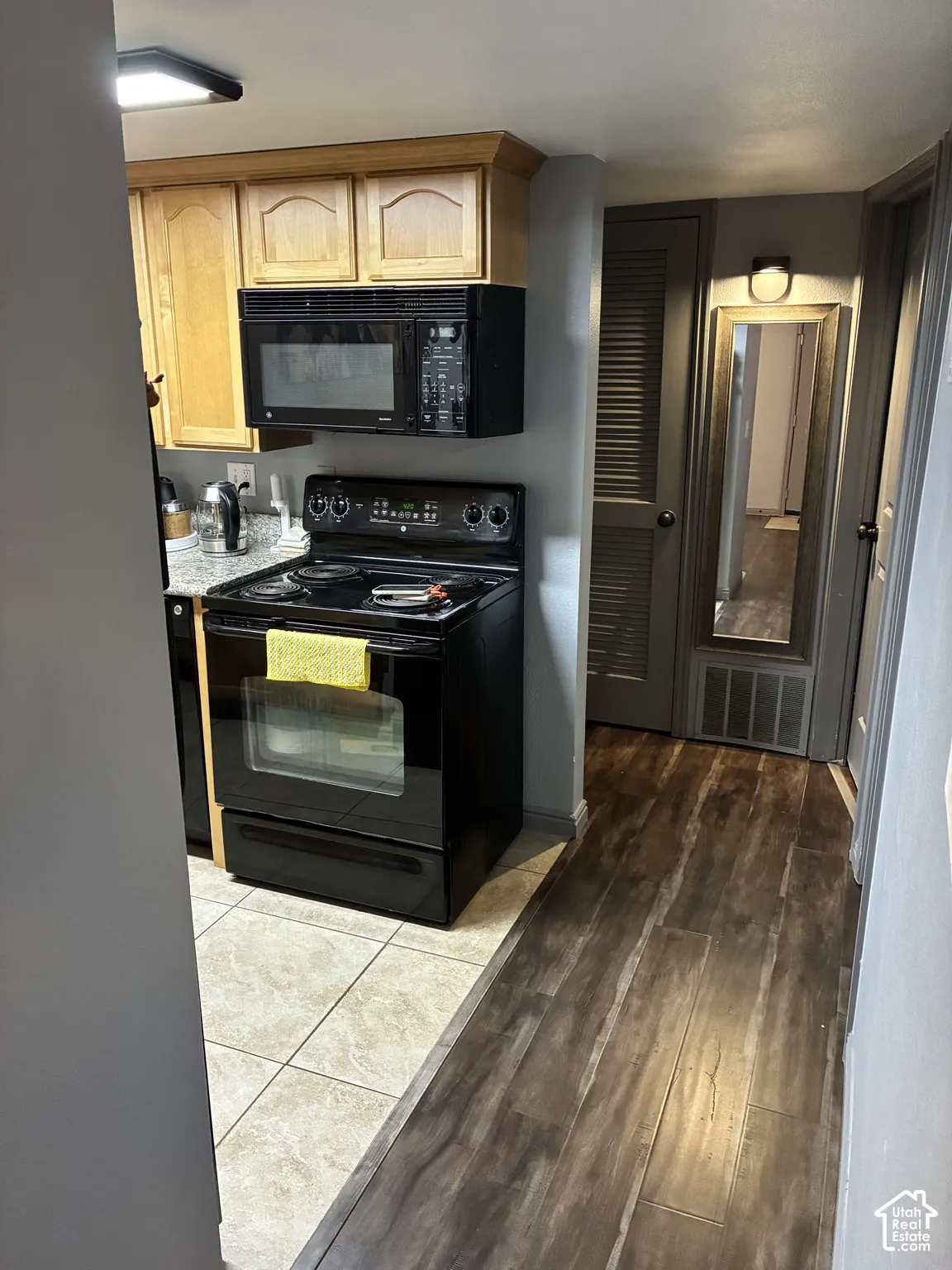 Kitchen featuring wood-finish cabinetry, stone-patterned countertops, a black electric range, a matching over-the-range microwave, and tile flooring