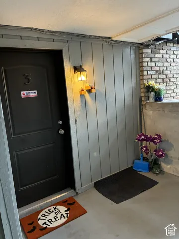 Covered entryway featuring vertical wood-style siding, a dark-finished door, and an attached wall-mounted lantern light fixture with a decorative brick accent wall