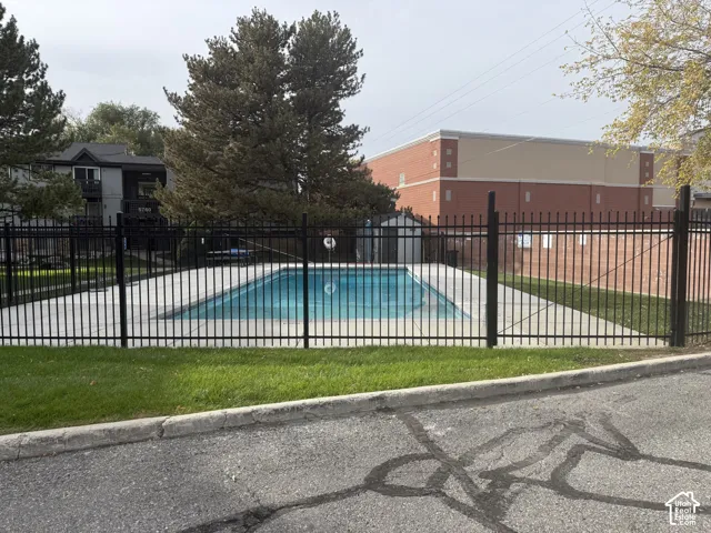 Rectangular swimming pool enclosed by metal security fencing, surrounded by a concrete deck and manicured lawn