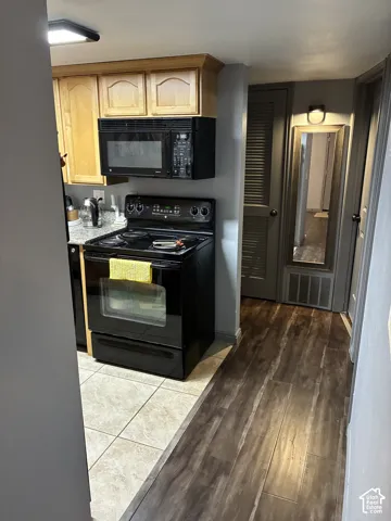 Kitchen featuring wood-finish cabinetry, stone-patterned countertops, a black electric range, a matching over-the-range microwave, and tile flooring