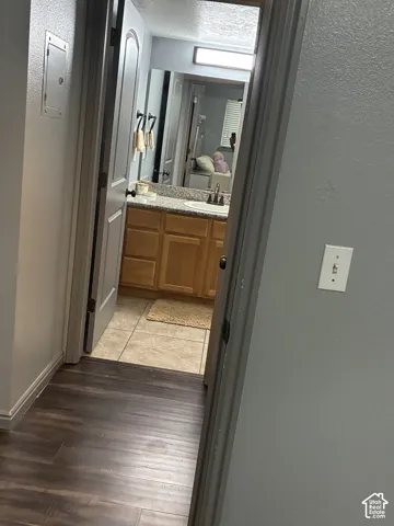 Bathroom featuring wood-finish flooring, a vanity with stone-composite countertop, integrated sink, and an over-mirror light fixture