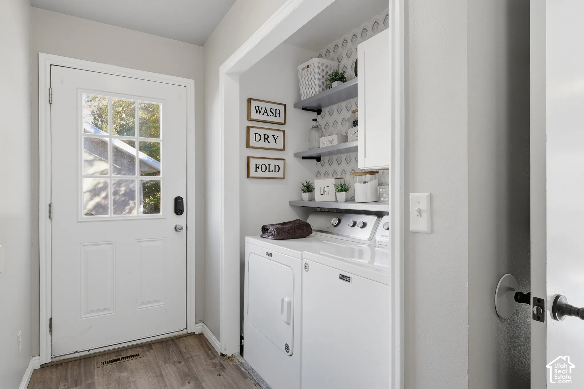 Laundry area featuring wood-finish flooring, white cabinetry, open shelving, and a patterned wall accent
