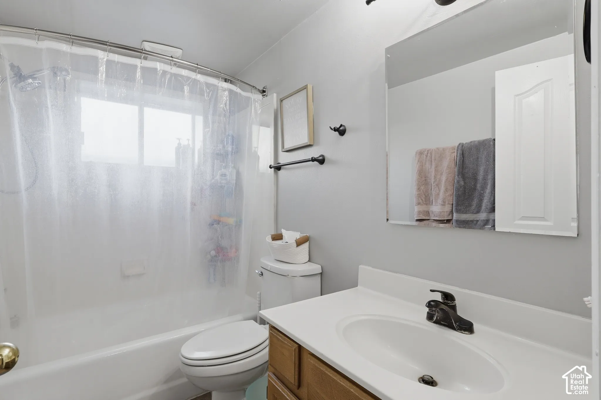 Bathroom featuring a vanity with a white countertop and integrated sink, matte black faucet hardware, a wall-mounted mirror, and a tub-shower combination