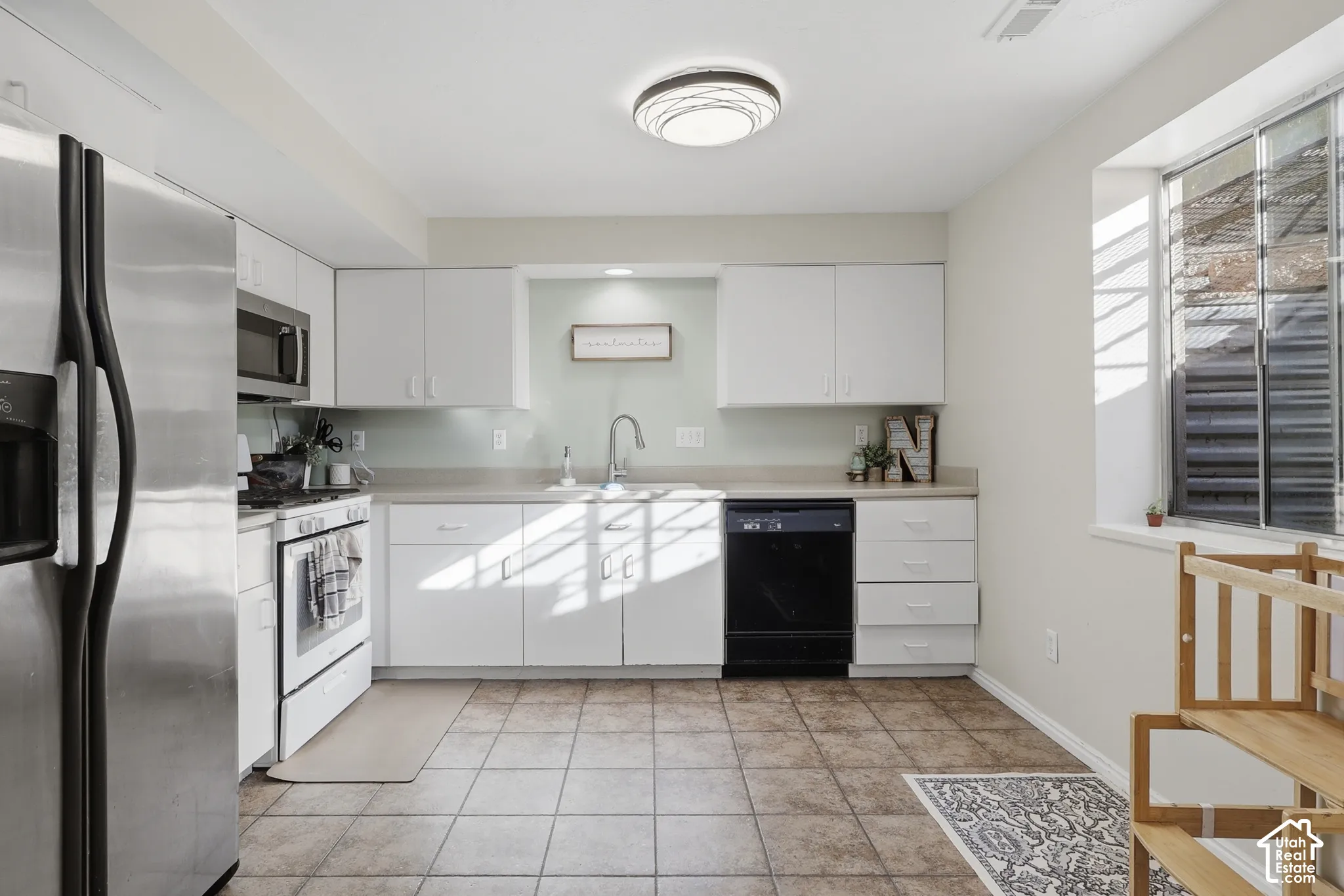 Kitchen featuring white cabinetry, stainless steel refrigerator, white range, tile flooring, and a large window