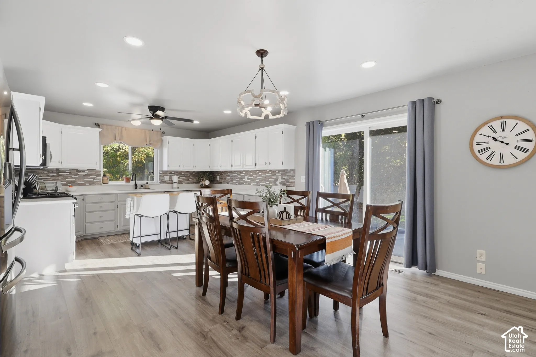 Kitchen and dining area featuring white cabinetry, stone-tiled backsplash, wood-finish flooring, recessed lighting, and sliding glass doors