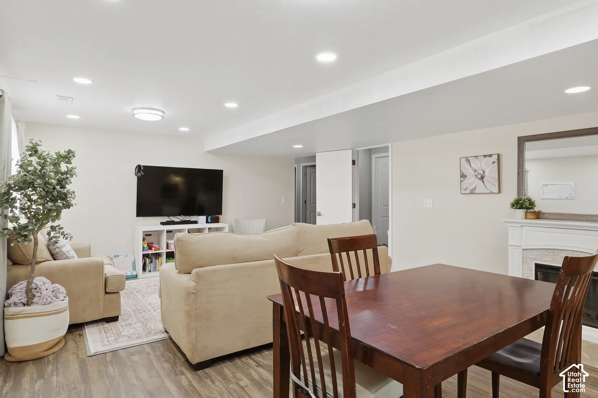 Recessed lighting, wood-finish flooring, and a fireplace featuring a white mantel with neutral-toned surround