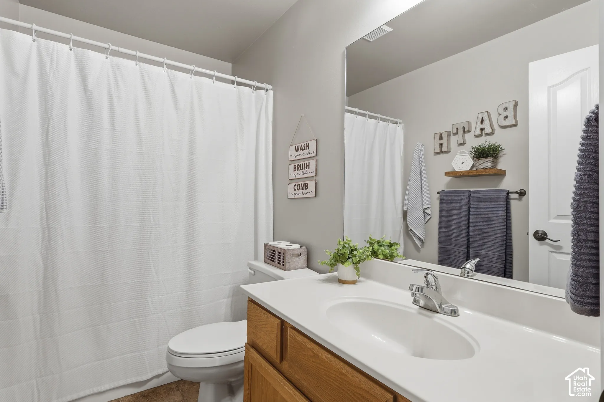 Bathroom featuring a wood-finish vanity cabinet, integrated sink countertop, large wall-mounted mirror, and a combination tub and shower with a curved curtain rod