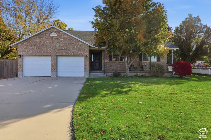 Single-story brick exterior featuring a covered front porch, two-car garage, concrete driveway, and mature landscaping