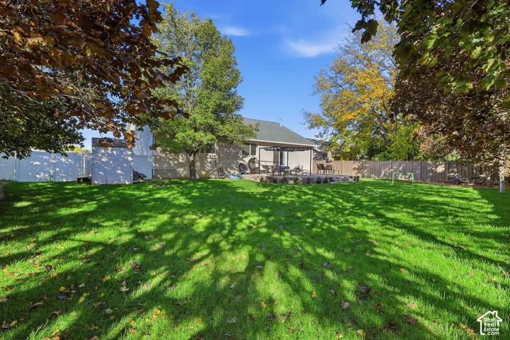 Expansive backyard featuring a sprawling lawn, mature trees, concrete patio, detached storage shed, and full-perimeter fencing