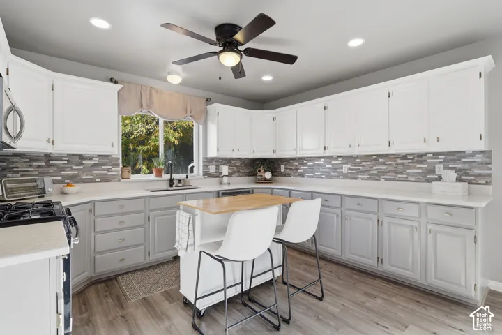Kitchen featuring two-tone cabinetry, multi-textured stone tile backsplash, wood-finish flooring, recessed lighting, and a ceiling fan