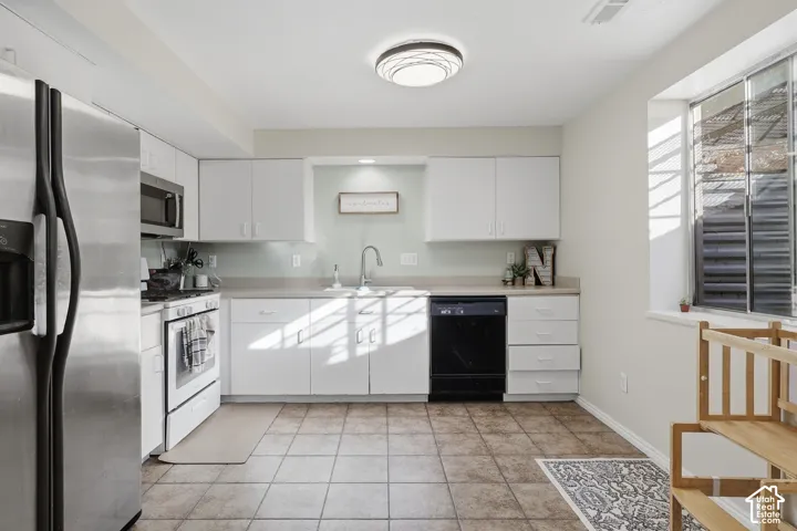 Kitchen featuring white cabinetry, stainless steel refrigerator, white range, tile flooring, and a large window