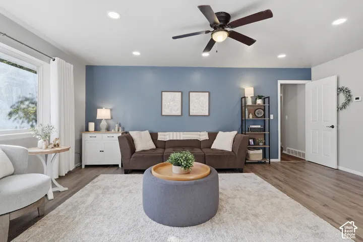 Living area featuring wood-finish flooring, recessed lighting, a ceiling fan with integrated light fixture, and an accent wall